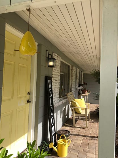A porch with yellow chairs and a table.
