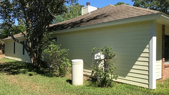 A white fire hydrant in the grass near a house.