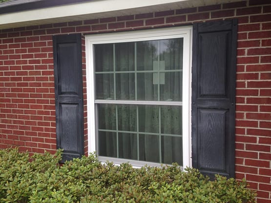 A window with shutters and a brick wall.