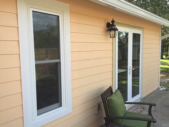 A yellow house with two windows and a green chair.