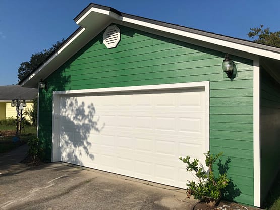 A green and white garage with a tree in front of it.