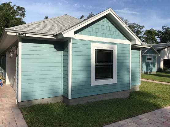 A blue house with grass around it and trees in the background.
